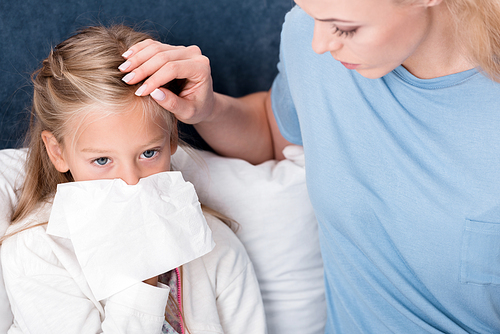 close-up shot of mother taking care of her daughter while she blowing nose