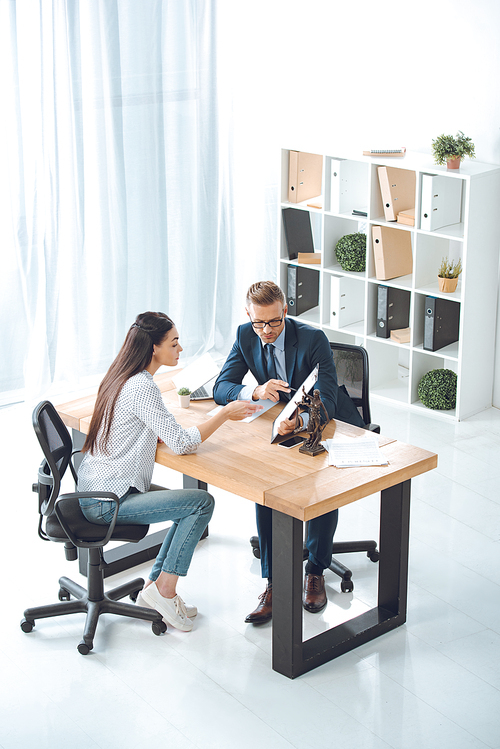 high angle view of lawyer pointing at clipboard and working with female client in office