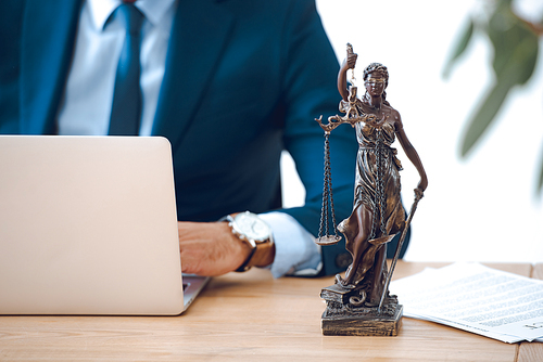 cropped shot of lawyer using laptop and lady justice statue on table