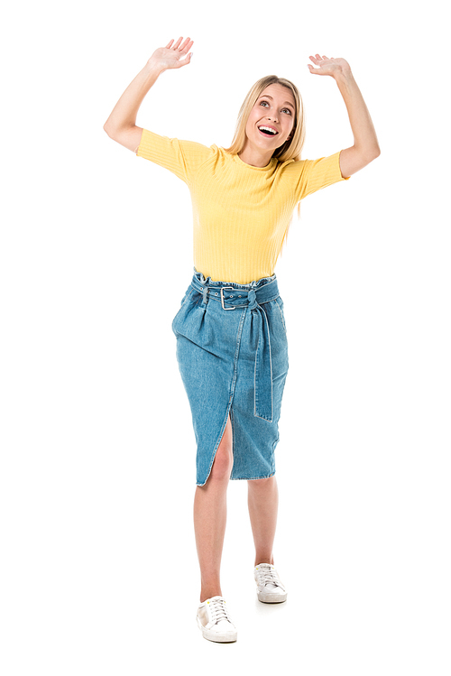 full length view of cheerful young woman raising hands and looking up isolated on white