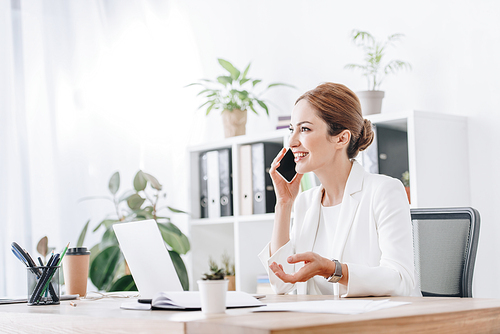 professional cheerful business woman talking on smartphone in modern office with laptop