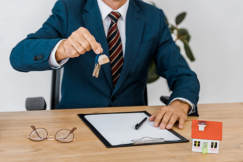 insurance agent holding keys with house model and glasses on table