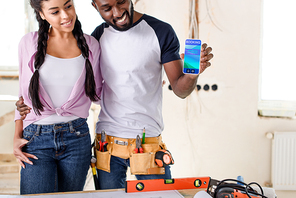 couple holding smartphone with booking app on screen during renovation