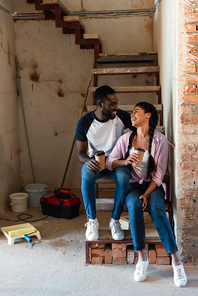 smiling african american couple resting with disposable cups of coffee during renovation at new home