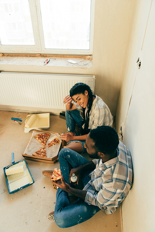 high angle view of african american couple eating pizza and drinking beer during renovation at home
