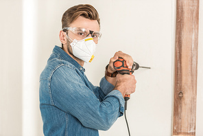 young man in protective workwear using electric drill and  during house repair