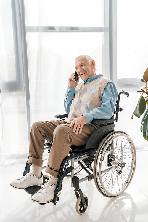 senior smiling man sitting in . and talking on smartphone in nursing home
