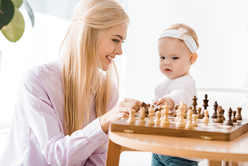 young cheerful mother teaching daughter playing chess