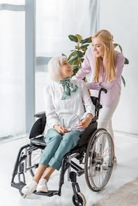 young woman speaking with senior woman in wheelchair at nursing home