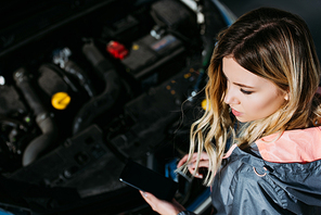 high angle view of young woman using smartphone with blank screen while repairing broken car