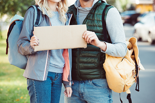 cropped shot of young couple with backpacks holding blank card on road