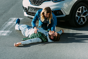 high angle view of scared young woman touching injured man lying on road after car accident