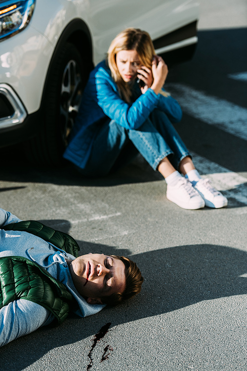 high angle view of scared young woman calling emergency while injured man lying on road after traffic collision