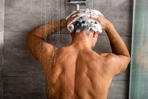 rear view of man washing hair with shampoo and taking shower