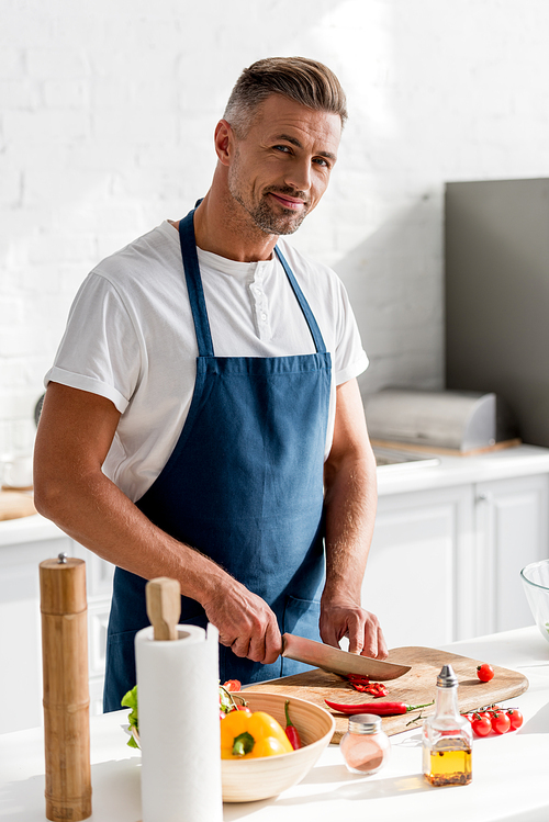 adult man cutting chili pepper on cutting board on kitchen