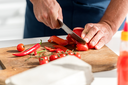 close up view of male hands cutting chili peppers on chopping board