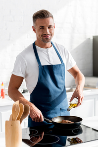 adult  smiling man pouring oil on steak at kitchen