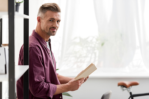 man standing with book in hands at home office