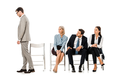 fired businessman going away while colleagues sitting on chairs and looking at him isolated on white