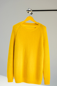 knitted yellow sweater on hanger at grey background
