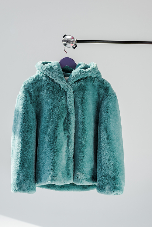 close up of fluffy green faux fur coat hanging on rack at grey background