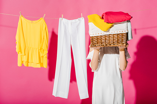 woman hiding face behind wicker basket with hanging clothes at background