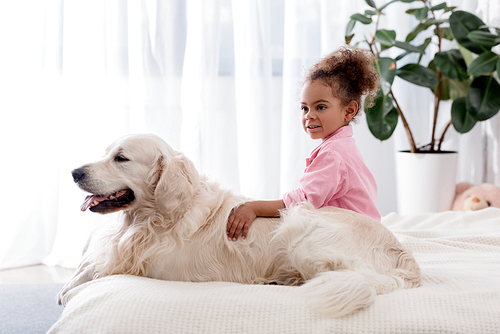 Adorable african american kid hugs her dog on the bed