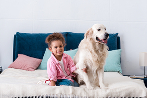 cute african american kid sitting on the bed and holds dog paw