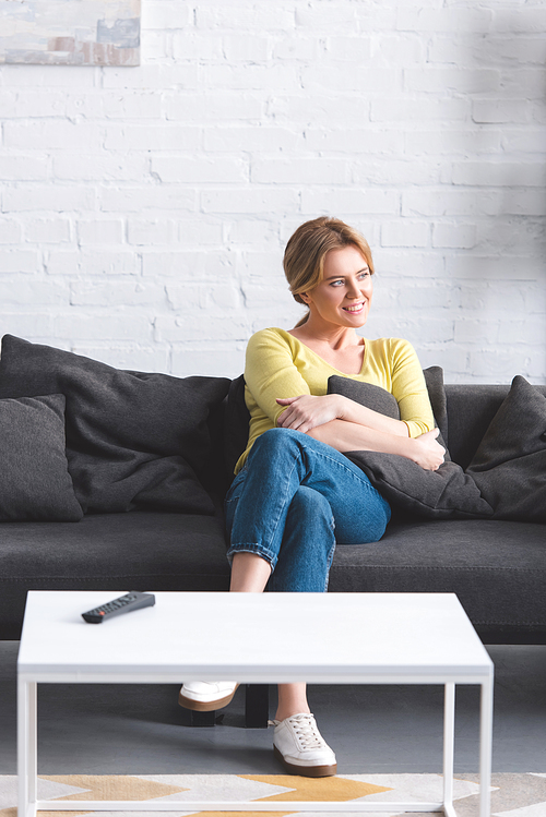 beautiful smiling woman sitting on couch and looking away at home