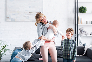 exhausted mother talking by smartphone and holding infant child while naughty siblings playing in room