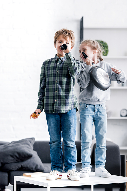 cute brother and sister having fun and singing with remote controller and frying pan