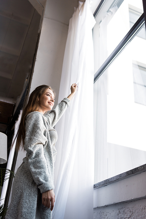 bottom view of girl standing near window and opening tulle