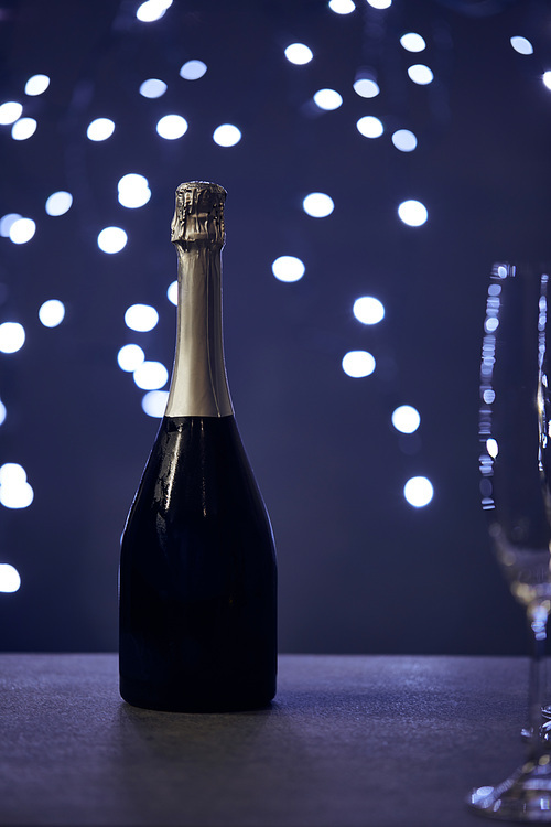 selective focus of champagne bottle and glass with christmas lights bokeh