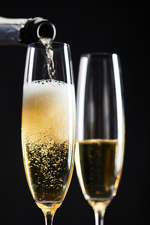 sparkling wine pouring from bottle into glasses for celebrating christmas, isolated on black