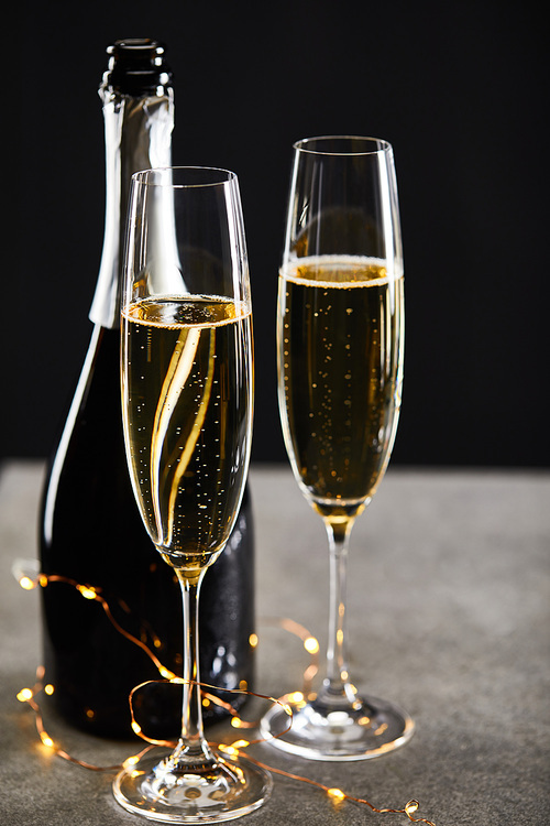 glasses and bottle with sparkling wine and yellow christmas lights, on black