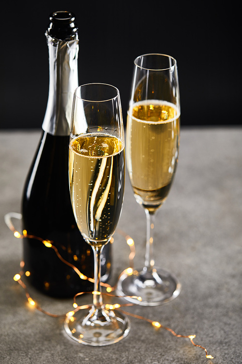 glasses and bottle with champagne and yellow christmas lights, on black