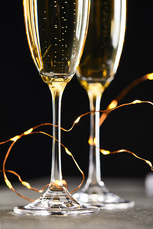 close up of traditional sparkling wine in glasses with yellow christmas lights, on black