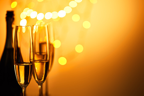 glasses and bottle of sparkling wine with yellow christmas lights bokeh