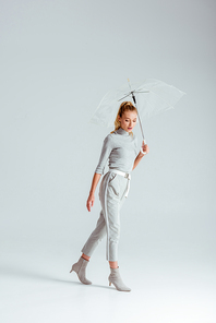 attractive woman in grey clothes posing with transparent umbrella on grey background