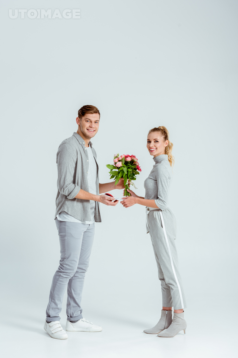 유토이미지 | man greeting woman with Valentines card and flower bouquet on grey background