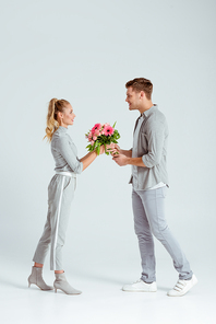 smiling man giving pink flower bouquet to woman isolated on grey background