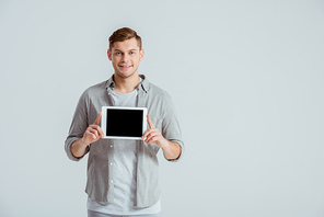 handsome man in grey clothing  and presenting digital tablet with blank screen isolated on grey