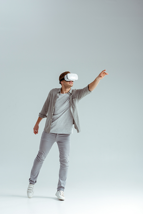 man in grey clothing gesturing while wearing virtual reality headset on grey background