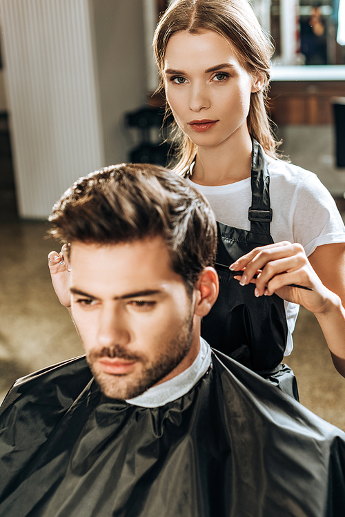 hairstylist  while cutting hair to handsome young man in beauty salon
