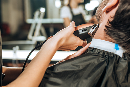 cropped shot of hairdresser using electric hair clipper and cutting beard to client in beauty salon