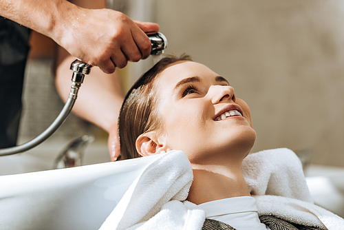 cropped shot of hairstylist washing hair to attractive smiling girl in beauty salon