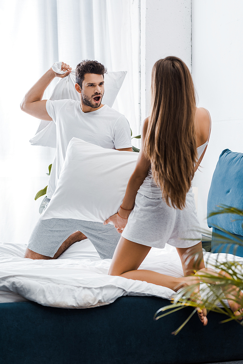 handsome man with funny face expression having pillow fight with girlfriend