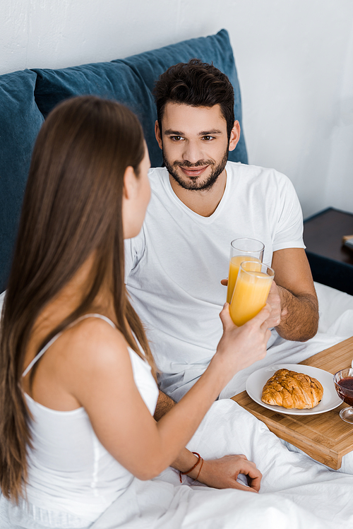 handsome man looking at girlfriend and clinking with glasses of orange juice