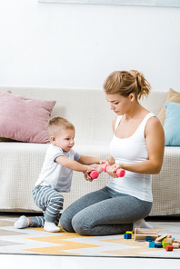 attractive woman holding dumbbells with cute toddler boy in living room