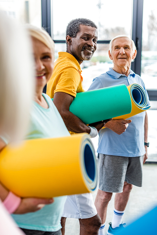 african american sportsman with fitness mat standing near friends at gym